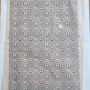 May include: A rectangular sheet of off-white fabric featuring a repeating pattern of red and green tulips enclosed in black oval frames with decorative borders. A circular coin is placed on the fabric to provide a sense of scale for the print.