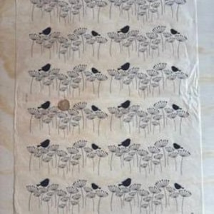 Puede incluir: Una hoja de papel blanquecino con un patrón repetido de pájaros negros posados ​​en diseños florales estilizados. El papel tiene una textura ligeramente arrugada y se ve una moneda en el centro.