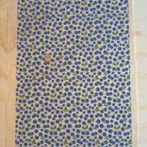 May include: A rectangular fabric panel featuring a pattern of blue blueberries and green leaves on a cream backdrop. A small, round, wooden button is attached. Suitable for crafts or home decor projects.