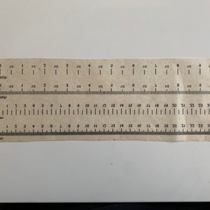 May include: A brown paper ruler with markings for both inches and centimeters. The ruler has a measurement scale of 10 inches and 54 centimeters.
