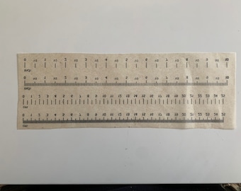 May include: A brown paper ruler with markings for both inches and centimeters. The ruler has a measurement scale of 10 inches and 54 centimeters.