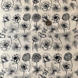 Puede incluir: Tela de estampado floral en blanco y negro con un patrón repetitivo de flores y hojas estilizadas. La tela tiene un fondo beige claro.