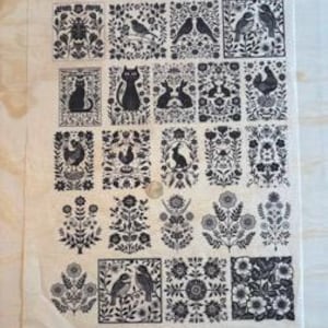 Puede incluir: Un paño de cocina de lino beige con un patrón repetido de ilustraciones de arte popular en blanco y negro. Los diseños incluyen pájaros, gatos, conejos, flores y otros elementos botánicos. El paño es rectangular y parece nuevo.