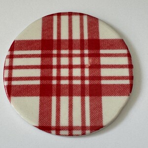 Może przedstawiać: Okrągła ceramiczna podkładka z czerwono-białym wzorem w kratkę.