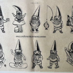 May include: A sheet of black and white ceramic transfer decals featuring 10 different gnome designs. The gnomes are depicted in various activities, including meditating, fishing, skiing, snowboarding, and ice skating. The text "www.ceramictransfers.com" is printed at the bottom of the sheet.