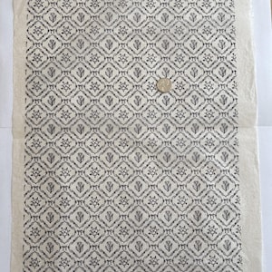 Könnte beinhalten: Ein rechteckiger Bogen aus cremefarbenem, strukturiertem Papier mit einem sich wiederholenden schwarzen Druckmuster aus rautenförmigen Rahmen, die abwechselnd florale Motive und Tulpenillustrationen enthalten, mit einer Münze als Größenvergleich.