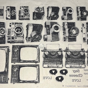 May include: A vintage-style digital collage featuring various images of cameras, typewriters, and televisions. The collage includes the words "Hello Cheese Say Love Bonjour Love Bonjour Say Cheese Love".