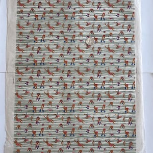 May include: A rectangular piece of fabric featuring a repeating pattern of small figures swimming and diving, set against a background of thin horizontal green stripes. A silver-coloured coin is placed on the fabric for scale reference.