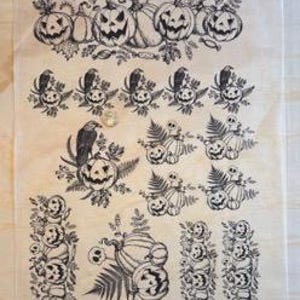 Op de afbeelding: Een vel tijdelijke Halloween-tattoos. De zwart-wit illustraties tonen pompoenen, schedels, raven en bladeren. De ontwerpen zijn gerangschikt in rijen en kolommen. Het vel ligt op een lichtgekleurd oppervlak.