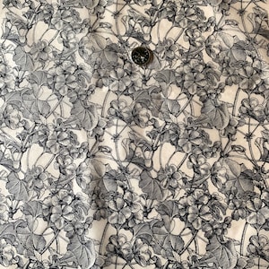 Può includere: Tessuto bianco con stampa floreale in bianco e nero. Il tessuto presenta un motivo ripetitivo di fiori e foglie stilizzati.