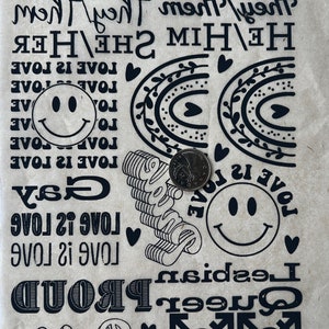 May include: Black and white stickers with various messages and symbols, including "Love is Love", "Gay", "Proud", "Queer", "Lesbian", "She/Her", "He/Him", "They/Them", and rainbow designs.