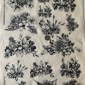Puede incluir: Una hoja de imágenes de sellos florales en blanco y negro. La hoja incluye una variedad de flores, incluyendo girasoles, lirios y margaritas. Las imágenes están impresas sobre un fondo de papel marrón claro.