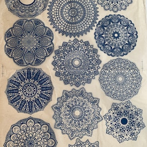 May include: Twelve blue lace doilies of varying sizes and patterns on a beige background. The doilies are all circular and have intricate designs. The text "布製レース模様装飾 01018350015A91  種類: 黒" is printed in black at the bottom right corner of the image.