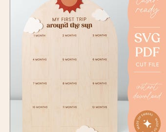 Puede incluir: Un letrero de madera para hitos de bebé con forma de arco con un sol y nubes. El letrero tiene 12 cuadrados para cada mes del año. El texto en el letrero dice "Mi primer viaje alrededor del sol".