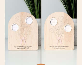 May include: Two variations of a wooden plaque with a floral design and space for four photos. The text "Thanks for helping us grow" and "Happy Mother's Day" is on the left plaque. The text "Your love gives us the strength to grow" and "Happy Mother's Day" is on the right plaque.