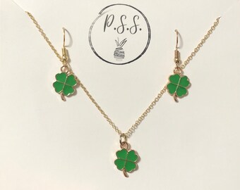 May include: A gold necklace and earrings set with green four-leaf clover charms. The necklace has a delicate chain and the earrings are dangle style.
