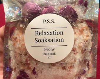 Könnte beinhalten: Eine durchsichtige Plastiktüte gefüllt mit weißen Badesalzen und rosa und violetten Blütenblättern. Die Tüte hat ein weißes Etikett mit der Aufschrift "P.S.S. Relaxation Soakstation Peony Bath Soak 3 oz."