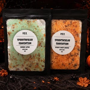 Pode incluir: Dois sacos pretos de sais de banho com janelas transparentes. O saco esquerdo contém cristais verdes rotulados P.S.S. SPOOKTACULAR SOAKSATION ZOMBIE LOTUS BATH SOAK 3OZ. O direito contém cristais laranja rotulados P.S.S. SPOOKTACULAR SOAKSATION SPOOKY SWEET ORANGE BATH SOAK 3OZ.