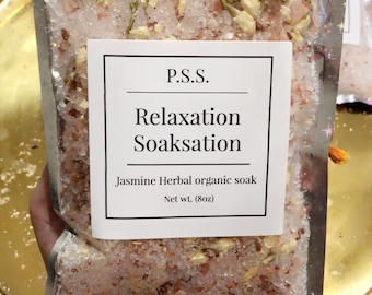 May include: A white pouch with a label that reads "P.S.S. Relaxation Soaksation Jasmine Herbal organic soak Net wt. (8oz)". The pouch contains a pink and white bath soak with white flower petals.