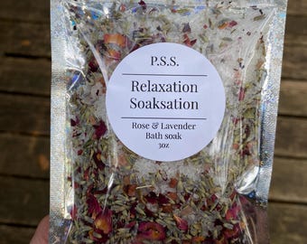 Könnte beinhalten: Ein klarer, holografischer Beutel gefüllt mit einem Rosen- und Lavendel-Badesalz. Der Beutel hat ein weißes rundes Etikett mit dem Text "P.S.S. Relaxation Soaksation" und "Rose & Lavender Bath soak 85g."