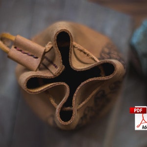 May include: A brown leather pouch with a drawstring closure. The pouch is folded in on itself, revealing the inside. The pouch has a decorative design on the outside.