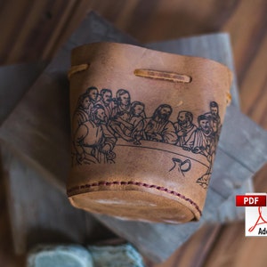 May include: A brown leather cup with a black and white illustration of the Last Supper. The cup has a red stitching detail around the top.