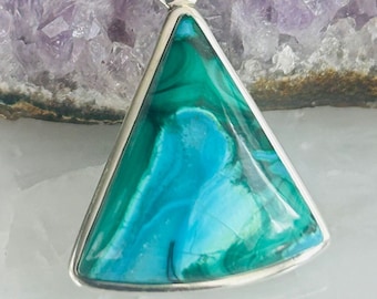 May include: A triangular pendant featuring a blue and green gemstone set in sterling silver. The pendant is displayed on a bed of amethyst crystals.