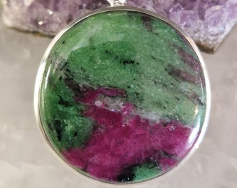 May include: A round green and pink gemstone pendant with a silver bail. The gemstone has a swirling pattern of green, pink, and black.