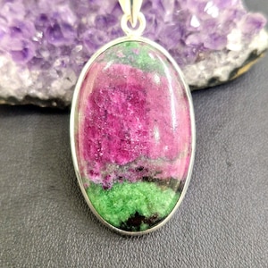 May include: A silver pendant featuring a green and pink oval-shaped gemstone. The gemstone has a layered appearance with shades of green, pink, and black.