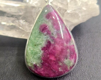 May include: A teardrop-shaped pendant with a green and pink gemstone set in silver.
