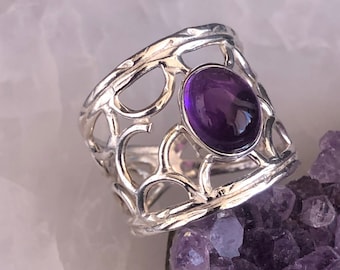 May include: A silver ring with a delicate, openwork design featuring a large, oval-shaped amethyst gemstone.