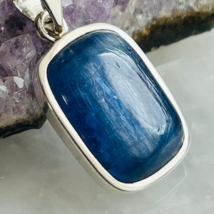 Peut inclure: Un pendentif en argent avec une pierre précieuse rectangulaire bleue. La pierre précieuse présente un motif strié et est sertie dans une bélière en argent.