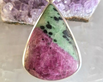 May include: A teardrop-shaped pendant with a green and pink gemstone set in silver. The gemstone has black flecks throughout.