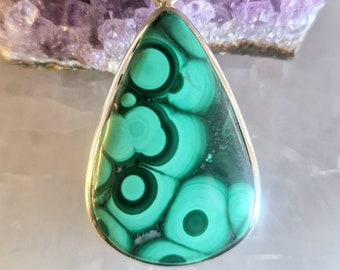 May include: A teardrop-shaped pendant featuring a green malachite stone set in sterling silver. The malachite has a swirling pattern of green and black.