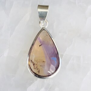 Puede incluir: Un colgante en forma de l&aacute;grima con una piedra preciosa p&uacute;rpura y marr&oacute;n engastada en un bisel de plata.