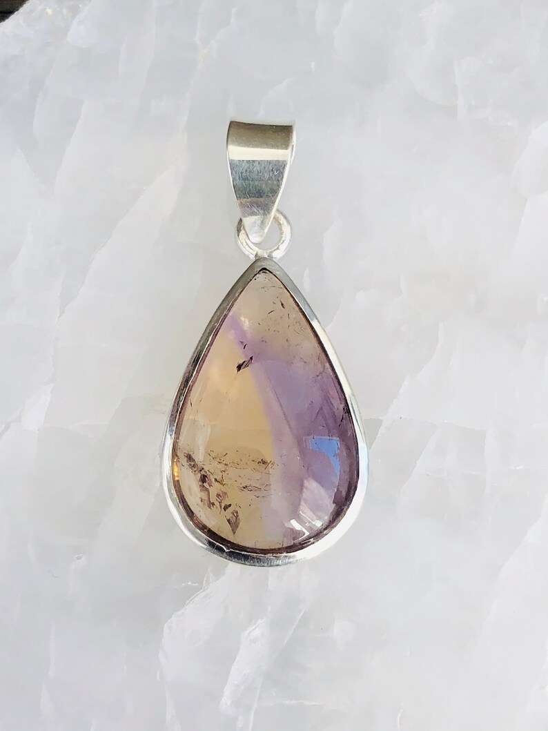 Puede incluir: Un colgante en forma de l&aacute;grima con una piedra preciosa p&uacute;rpura y marr&oacute;n engastada en un bisel de plata.