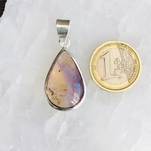 Puede incluir: Un colgante en forma de l&aacute;grima con una piedra preciosa p&uacute;rpura y amarilla engastada en plata. El colgante es aproximadamente del tama&ntilde;o de una moneda de euro.