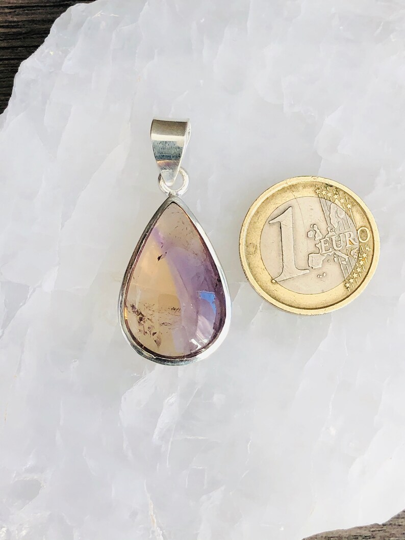 Puede incluir: Un colgante en forma de l&aacute;grima con una piedra preciosa p&uacute;rpura y amarilla engastada en plata. El colgante es aproximadamente del tama&ntilde;o de una moneda de euro.