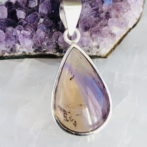 Puede incluir: Un colgante en forma de l&aacute;grima con una piedra preciosa transparente, p&uacute;rpura y marr&oacute;n engastada en un marco de plata.
