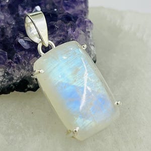 May include: A silver pendant featuring a rectangular moonstone with a blue iridescent sheen.