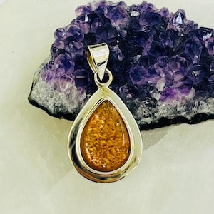 Op de afbeelding: Een traanvormige hanger met een zilveren zetting en een gouden sunstone edelsteen.
