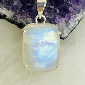 May include: A silver pendant with a large, rectangular, iridescent moonstone. The stone has a blue and white color with a shimmery effect.