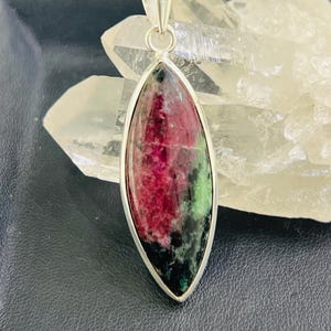 Puede incluir: Un colgante de plata con una piedra preciosa verde y rosa en forma de lágrima.