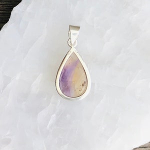Puede incluir: Un colgante en forma de l&aacute;grima con una piedra de fluorita p&uacute;rpura y amarilla engastada en plata de ley.