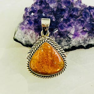 Op de afbeelding: Een zilveren hanger met een driehoekige oranje sunstone edelsteen, gezet in een touwachtige rand.