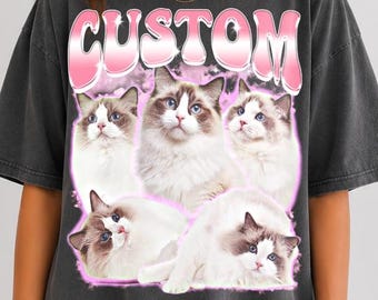 May include: A charcoal gray short-sleeve t-shirt featuring the word CUSTOM in large pink gradient letters at the top. Below the text are five images of fluffy white and brown ragdoll cats arranged in a collage, surrounded by a soft pink glow.