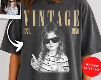 May include: A charcoal gray oversized t-shirt featuring a large black and white photographic print of a child wearing sunglasses and a striped shirt. The text VINTAGE EST. 1986 is printed in a tan serif font above the child. A small inset photo shows the same child.