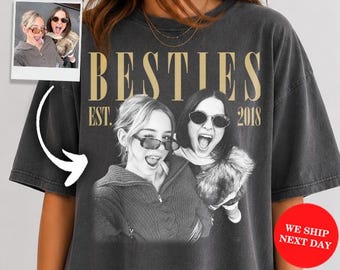 May include: A charcoal gray oversized t-shirt featuring a black and white graphic of two people wearing sunglasses with the text BESTIES EST. 2018. The shirt includes a small inset photo showing the same two people and a red circular graphic.