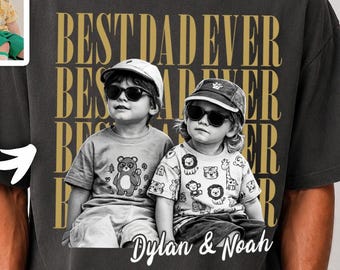 May include: A charcoal gray short-sleeve t-shirt featuring a large graphic print of two children wearing caps and sunglasses. The text BEST DAD EVER is repeated in gold behind the children, with the names Dylan & Noah printed in white script below.