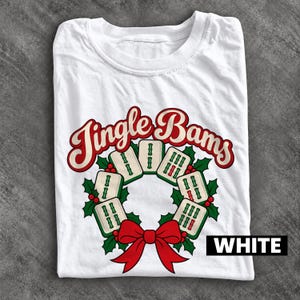 Puede incluir: Una camiseta blanca con un gráfico de una corona navideña hecha de fichas de mahjong. El texto Jingle Bams está impreso en rojo y crema sobre la corona, decorada con hojas de acebo verdes, bayas rojas y un gran lazo rojo.